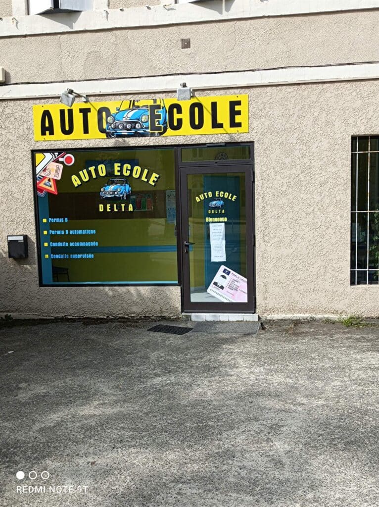 Auto Ecole Delta: panneau jaune "AUTO ECOLE" avec Mini bleue. Vitrine liste Permis B, automatique, conduite accompagnée et supervisée. Permis de conduire visible.