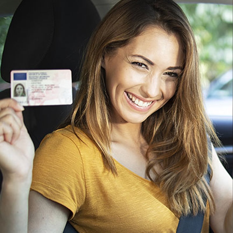 Jeune femme souriante dans une voiture, montrant fièrement son nouveau permis de conduire européen. Elle est visiblement heureuse.